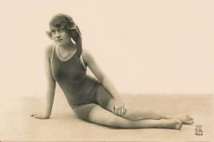 arcade-card-french-woman-in-head-scarf-and-wooly-bathing-suit-sitting-on-beach-leaning-on-one-arm-1920s